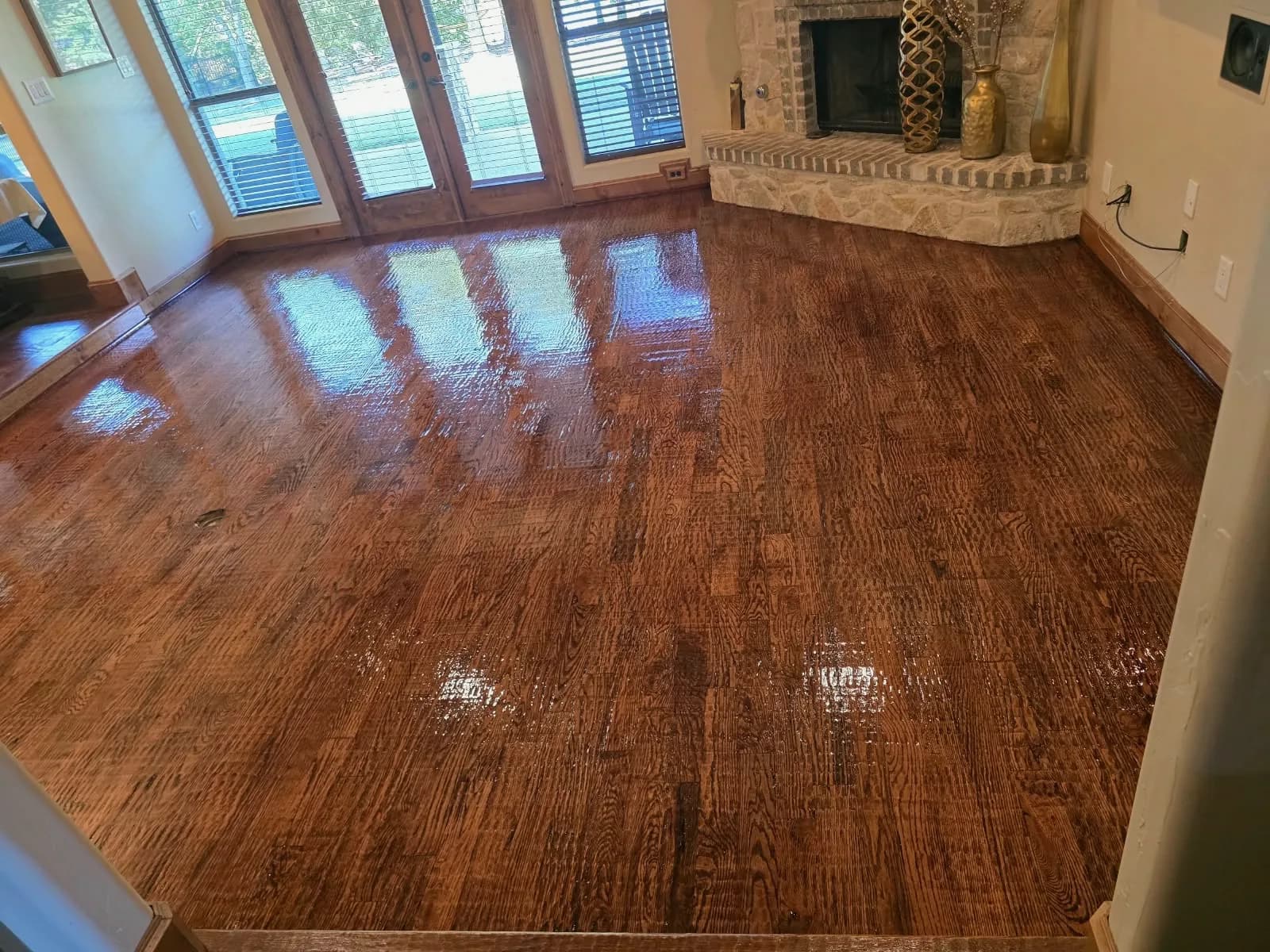 Hand-scraped solid wood floor in progress in a Wylie, TX living room with a stone corner fireplace and French doors